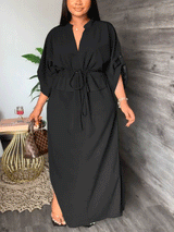Woman wearing a long black dress with a v-neck, drawstring waist, and side slits.