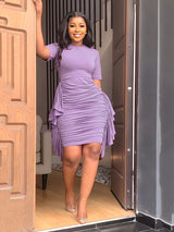 Woman in a purple ruched dress smiling and standing in a doorway.