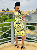 Woman wearing a yellow newspaper print t-shirt dress with black strappy heels, standing on a balcony.