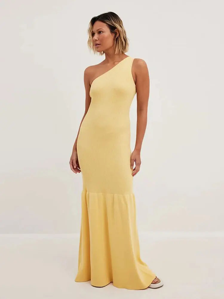 Model wearing a yellow one-shoulder ribbed knit maxi dress with a mermaid hem, standing against a white background.