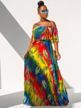 Woman wearing a vibrant rainbow gradient off-the-shoulder maxi dress with a tropical leaf print, standing against a white wall with shadows.