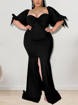 Woman wearing a black mermaid gown with puffed sleeves and a high slit