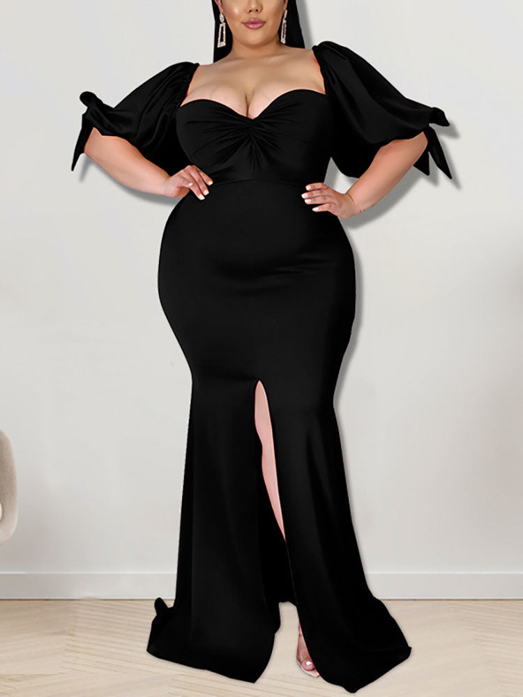 Woman wearing a black mermaid gown with puffed sleeves and a high slit