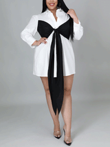 Full-length shot of a plus-size woman in a white shirt dress with a black bow, showcasing the dress from the front.