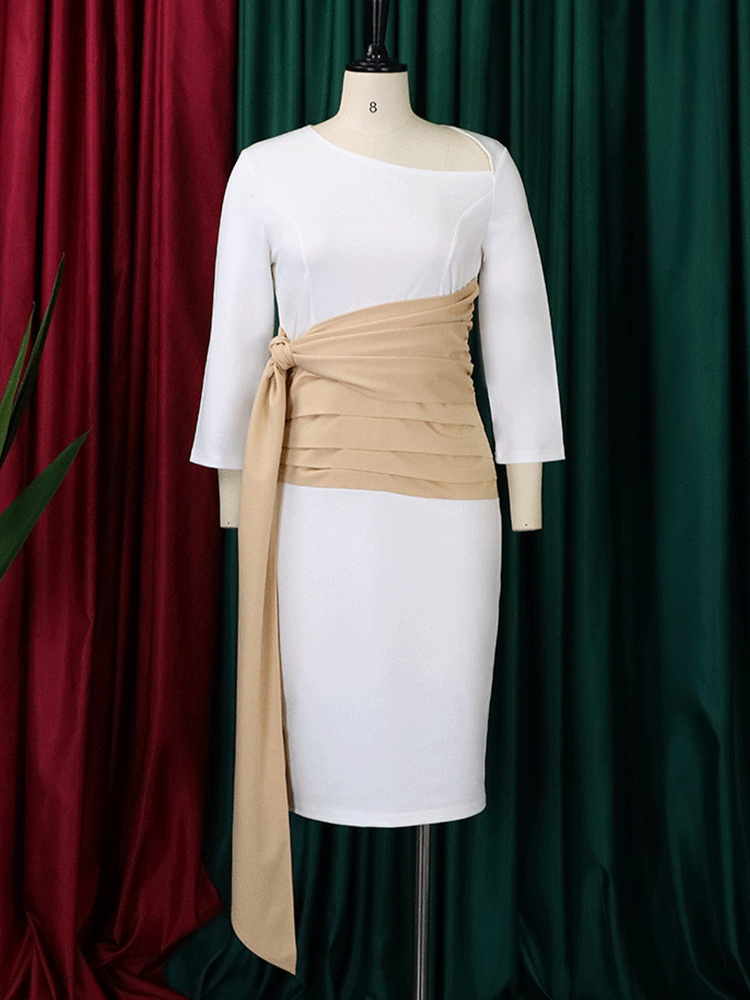 White sheath dress with a tan ruched sash and tie detail displayed on a mannequin against a backdrop of burgundy and green curtains.