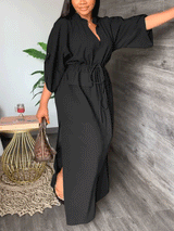Woman in a black maxi dress with batwing sleeves and a cinched waist.