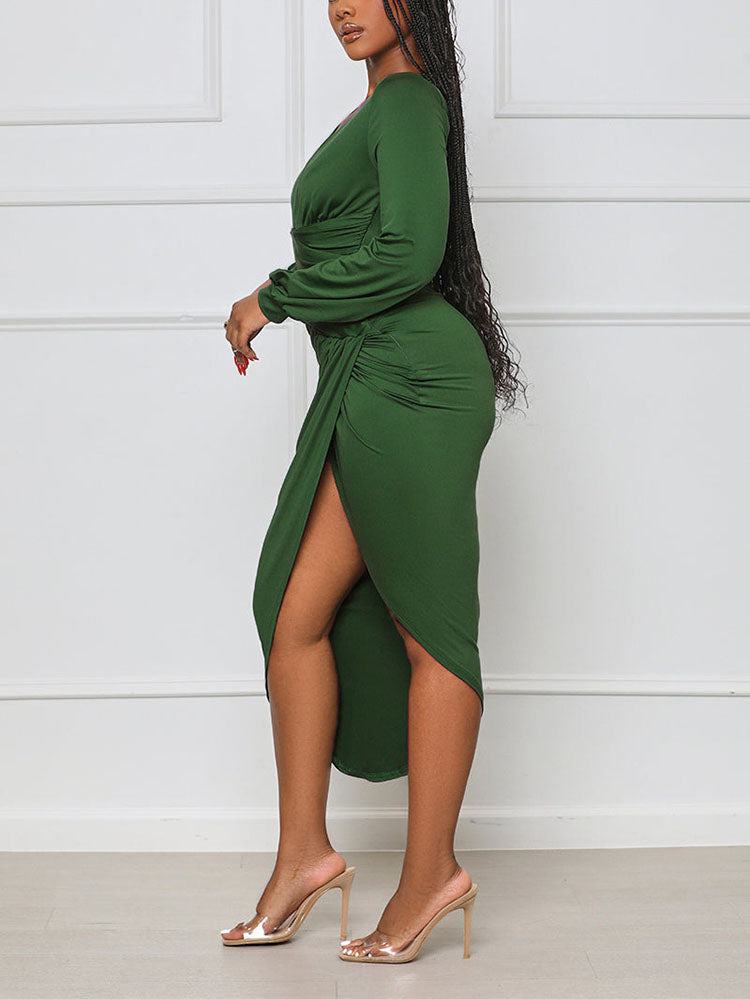 Side view of a woman in a green long-sleeve ruched V-neck dress with an asymmetrical hem and high slit.