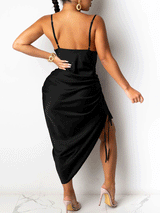 Back view of a woman in a black satin midi dress with spaghetti straps and an asymmetrical hemline.
