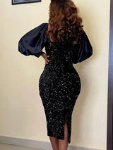 Back view of a woman in a black sequined midi dress with long puff sleeves and a square neckline, showing the slit detail.