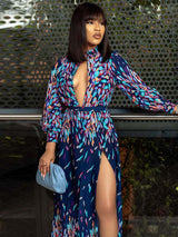 Close-up of a woman in a long, navy blue maxi dress with a colorful abstract print, high neckline, deep V-cutout, and long sleeves.