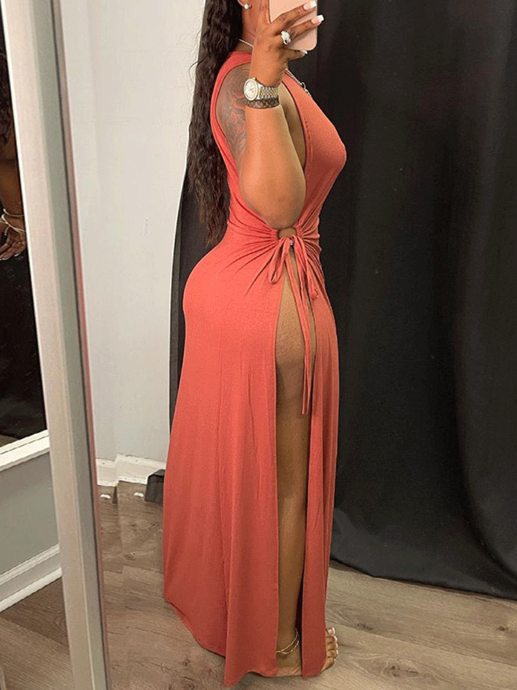 Side view of a woman wearing a rust-colored sleeveless maxi dress with a high slit and tie detail.