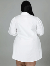 Back view of a plus-size woman wearing a white shirt dress, showing the puff sleeves and hemline.