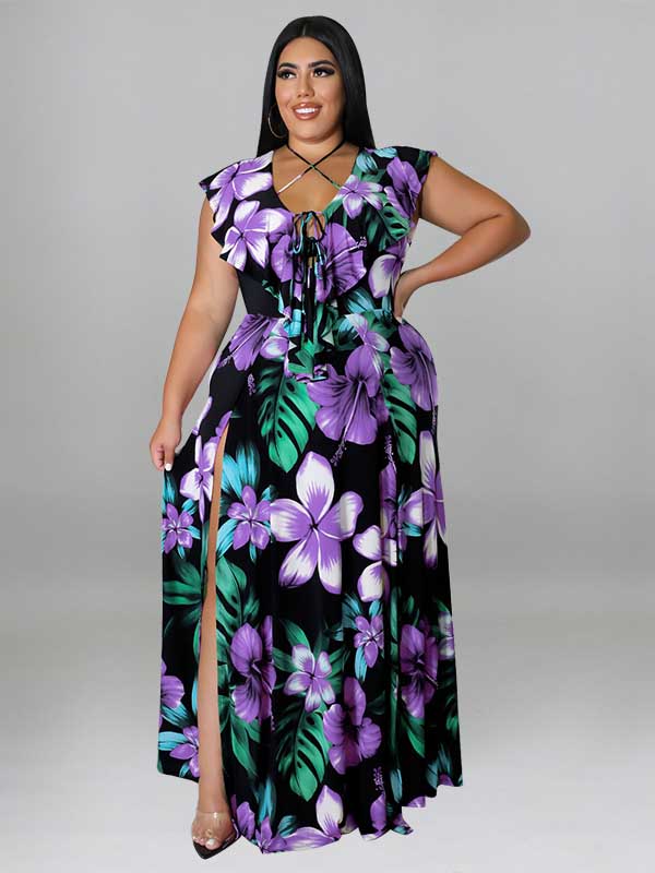 Woman wearing a black maxi dress with a purple and green floral print, featuring a V-neck with lace-up detail and a high slit.