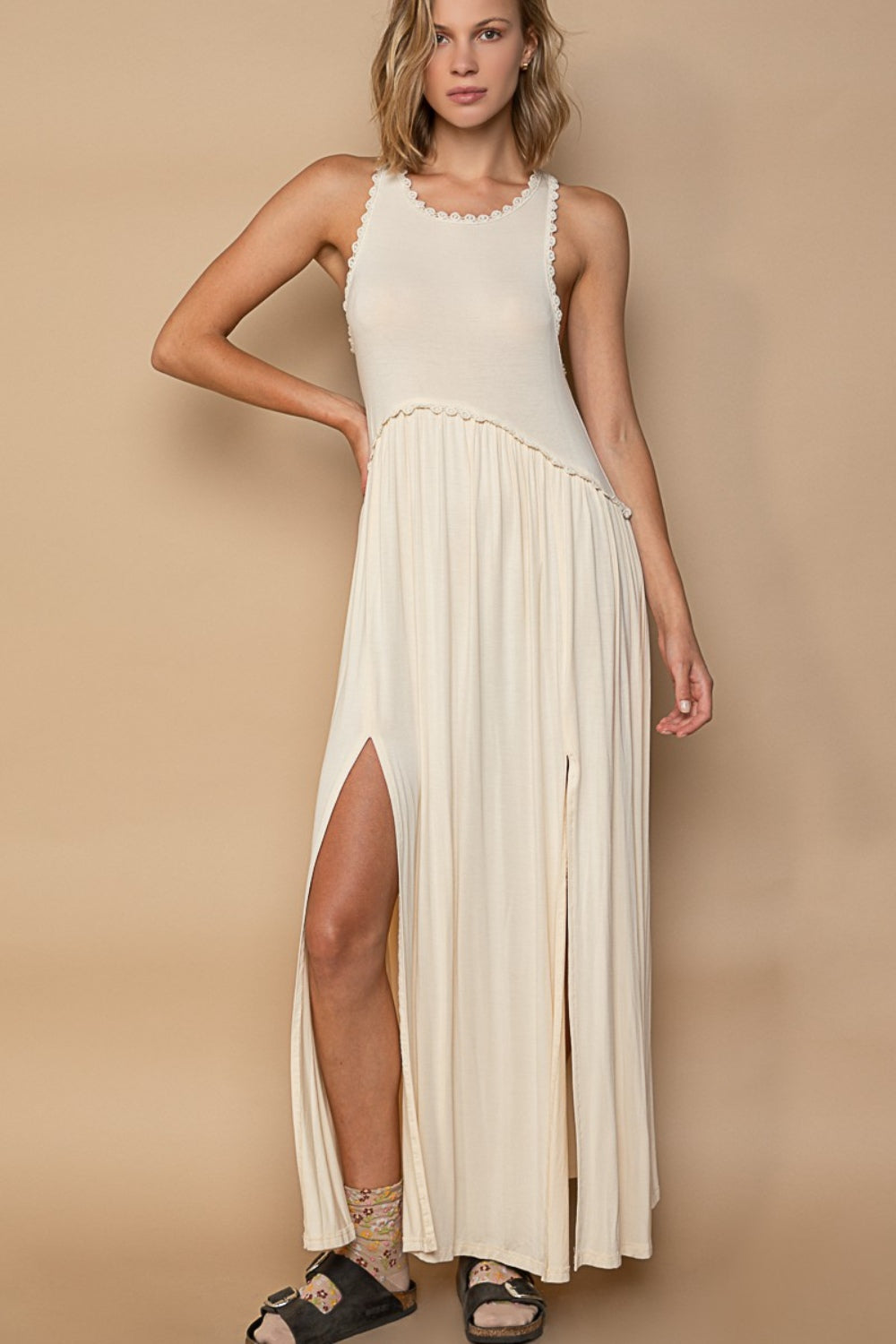 Woman wearing a cream-colored sleeveless maxi dress with high slits and scalloped trim