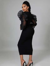 Back view of a woman in a black midi dress with sheer puff sleeves