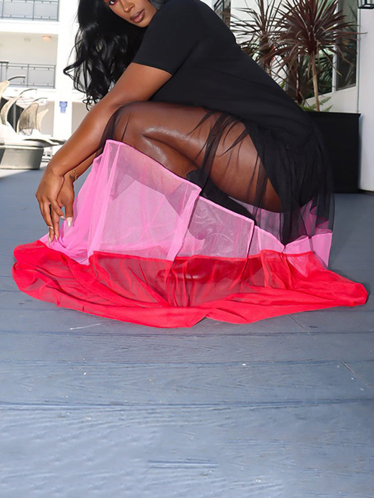 Close-up of a woman's legs wearing a black dress with a sheer, layered mesh skirt in pink and red, demonstrating the transparency.