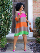 A woman poses in front of a brick house wearing a striped A-line dress and colorful heels.