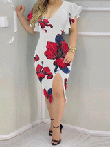 Woman wearing a white bodycon midi dress with a red and blue floral print, V-neckline, ruffle sleeves, and a high slit, accessorized with gold bracelets.