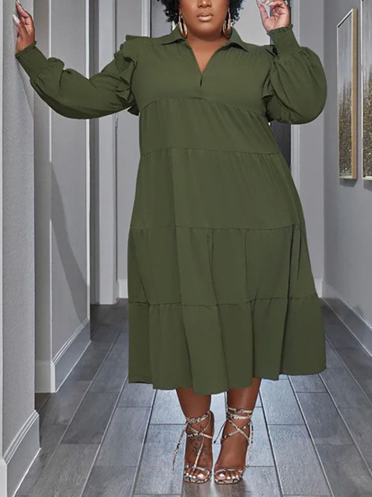 Plus-size model wearing a green tiered midi dress with voluminous sleeves and ruffled shoulders.