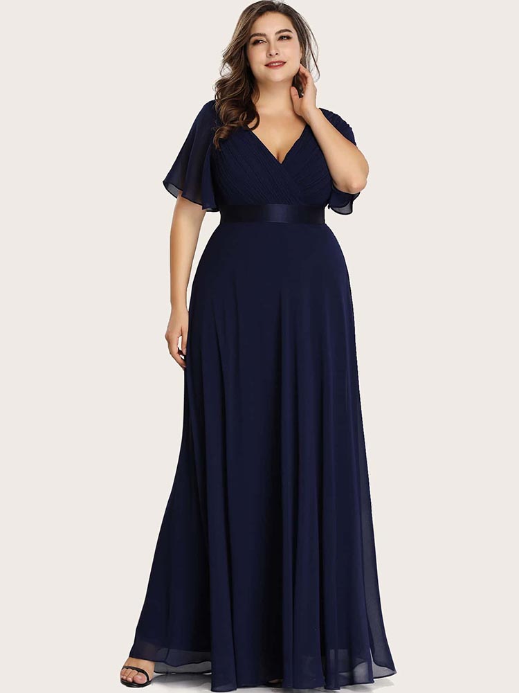 Woman in a navy blue formal dress with a pleated bodice and empire waist, looking elegantly to the side.