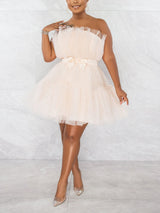 Full-body shot of a woman in a short, strapless, tiered tulle dress with a satin bow at the waist, paired with sparkling heels.