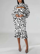 Woman wearing a black and white leopard print knit dress with a high neck, cut-out detail, long puff sleeves, and a mermaid hemline, posing with hands on hips.