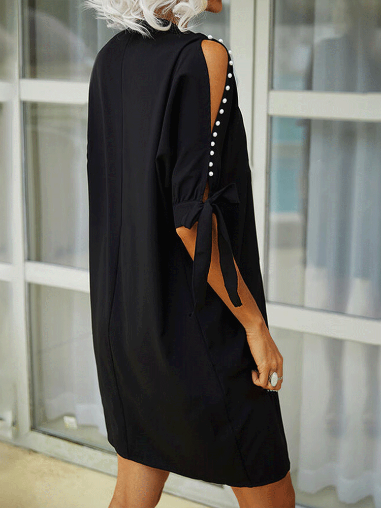 Back view of a woman in a black shift dress with a simple silhouette and cut-out sleeves.