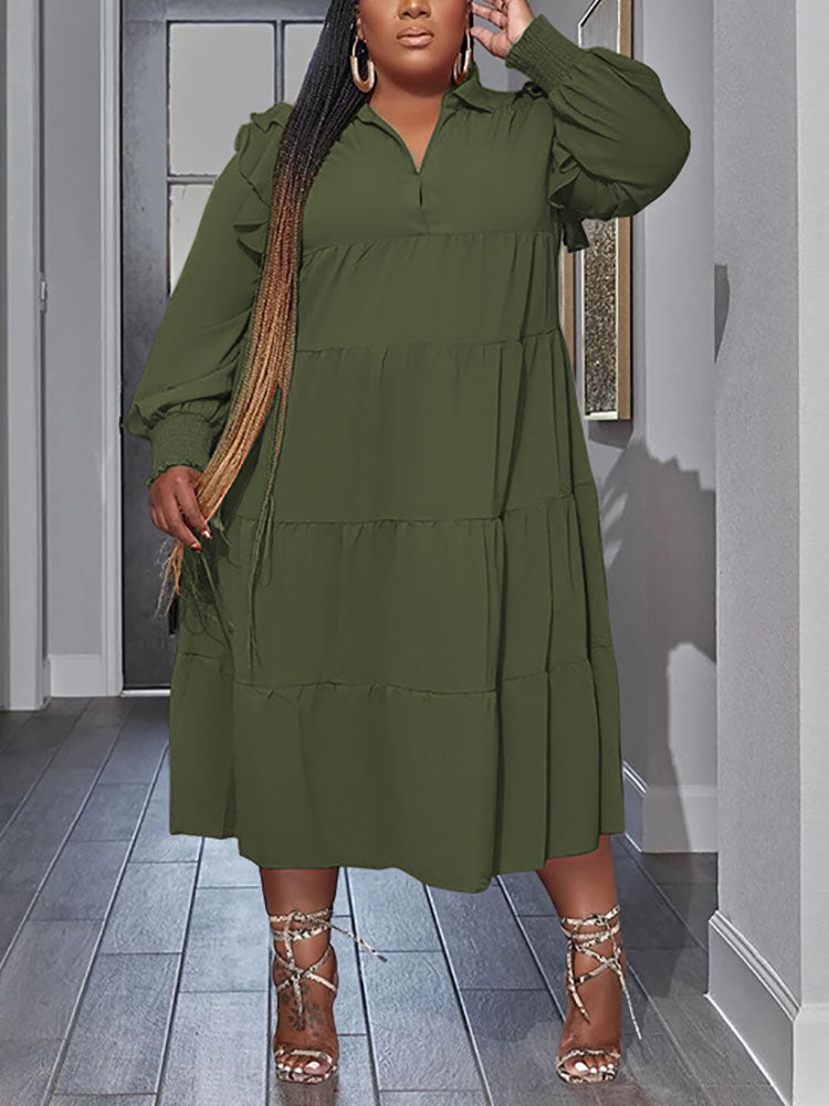 Plus-size model wearing a green tiered midi dress with voluminous sleeves and long braided hair.