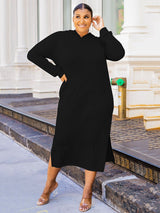 Woman wearing a black midi hooded dress with side slits and pockets, standing on a sidewalk.