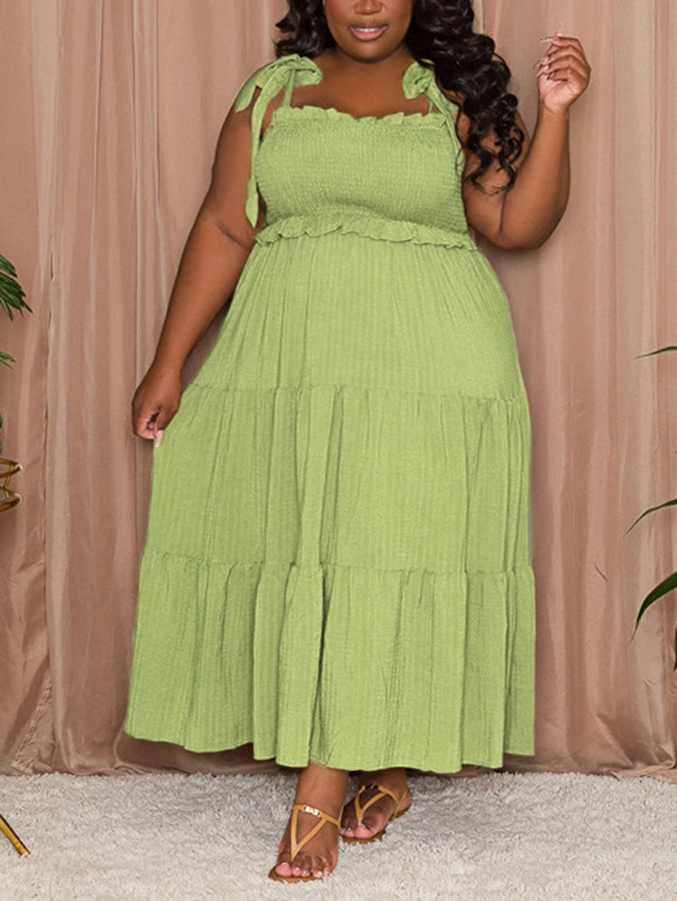 Plus-size woman wearing a lime green tiered maxi dress with tie shoulder straps and a smocked bodice, standing indoors.