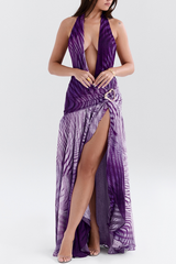 Woman posing in a purple printed halter neck gown with a deep V-neck and a side slit.