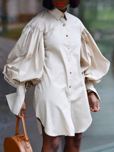 Woman wearing a beige oversized shirt dress with dramatic balloon sleeves and a round tan handbag.