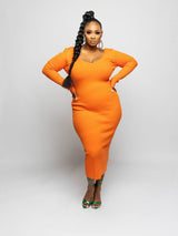 Woman in an orange ribbed knit midi dress with long sleeves and a V-neckline, posing with hands on hips and a braid.