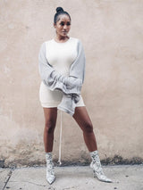 Woman wearing a white mini dress with grey voluminous sleeves and patterned boots.