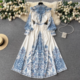 Overhead view of the white maxi dress with blue paisley print, positioned alongside a straw hat and a pearl-adorned handbag.