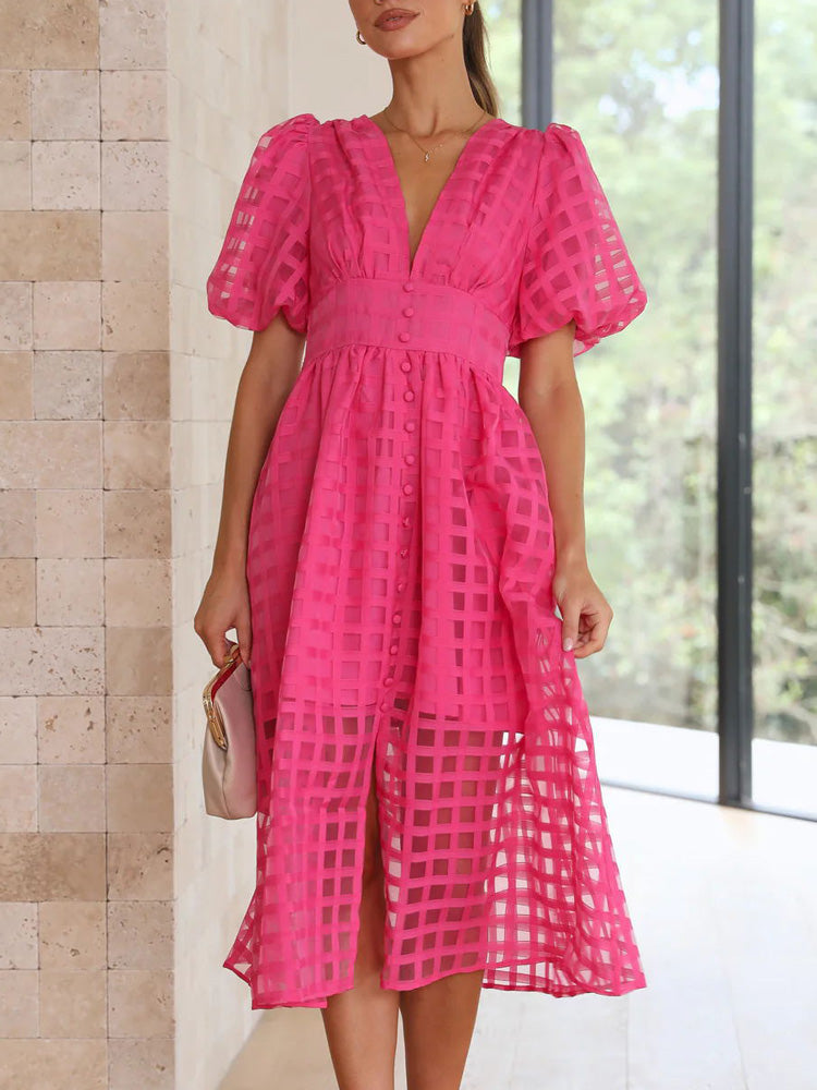 Woman in a bright pink midi dress with puff sleeves and a grid pattern overlay, holding a small cream handbag.