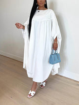 Woman wearing a white maxi dress with flowy sleeves and white sandals, holding a blue handbag