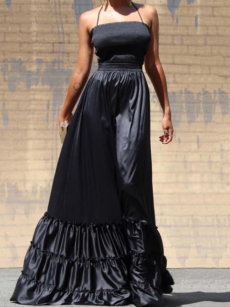 Full body shot of a woman wearing a black satin maxi dress with a ruffled hem, standing against a textured wall.