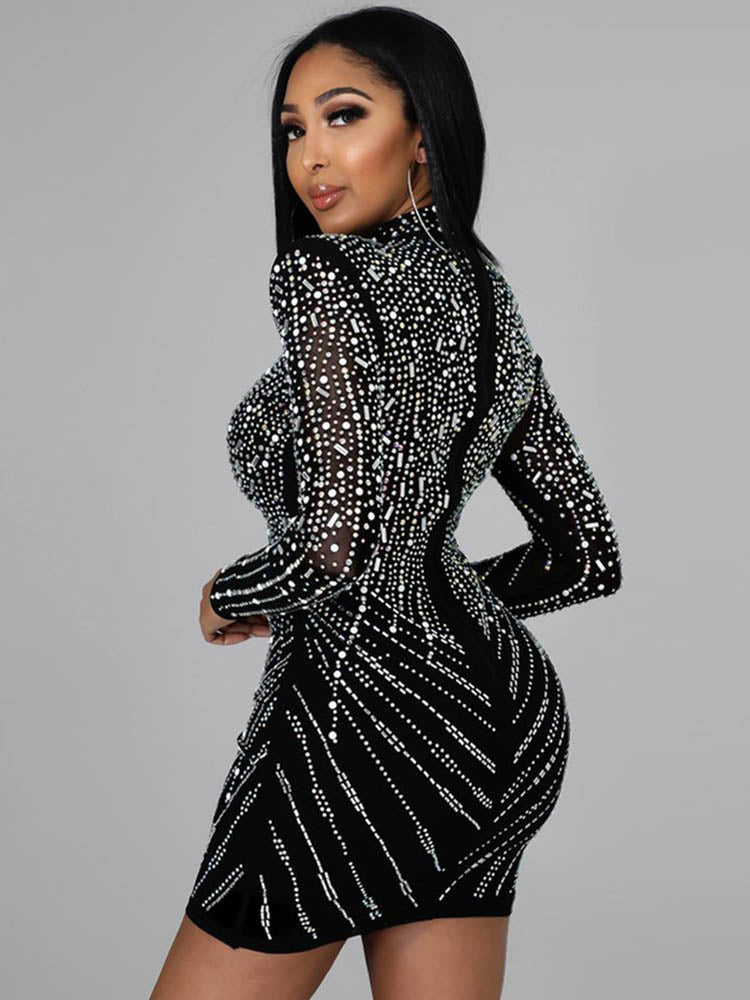 Rear view of a woman in a black long-sleeved mini dress with rhinestone embellishments. The dress has a figure-hugging silhouette and a high neckline.
