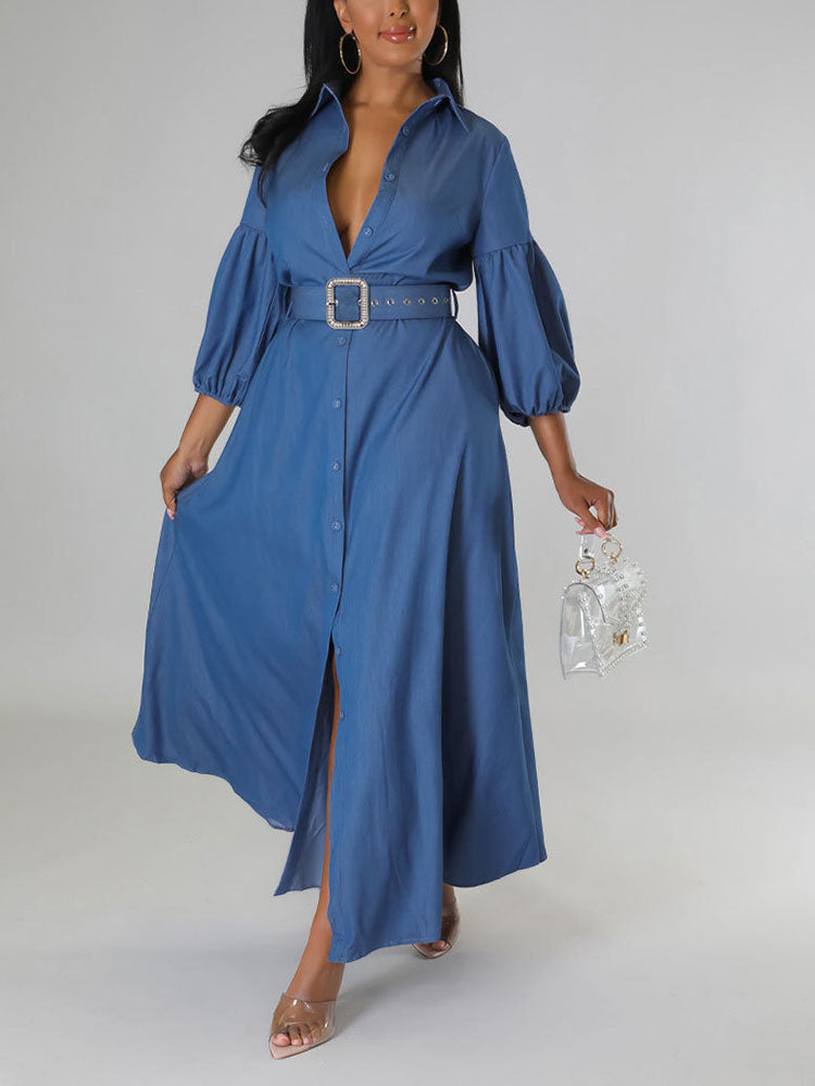 Woman wearing a blue denim maxi dress with puffed sleeves and a belted waist, holding a clear handbag.