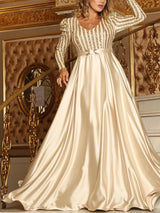 Woman wearing a champagne long-sleeved A-line formal dress with a sequined striped bodice and a satin skirt.