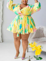 Plus-size woman wearing a yellow tie-dye mini dress with a V-neck and full sleeves, posing indoors with hands raised.