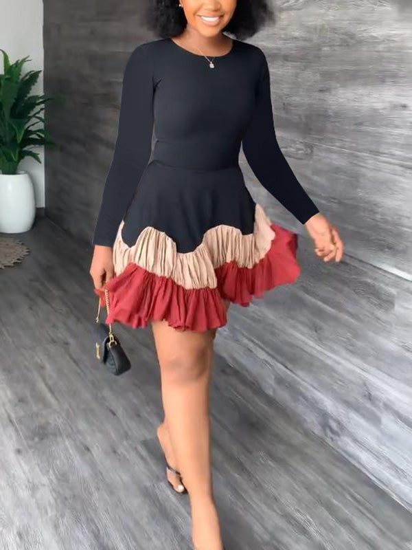 Woman wearing a black long-sleeved dress with a tiered, ruffled hem in shades of red and tan.