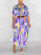 Woman wearing a long, light purple collared shirt dress with a colorful graphic print of people, cinched with a brown belt.
