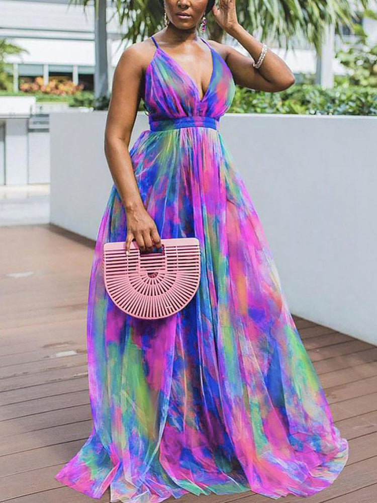 Woman posing in a vibrant tie-dye maxi dress with a slit, holding a pink fan-shaped purse.