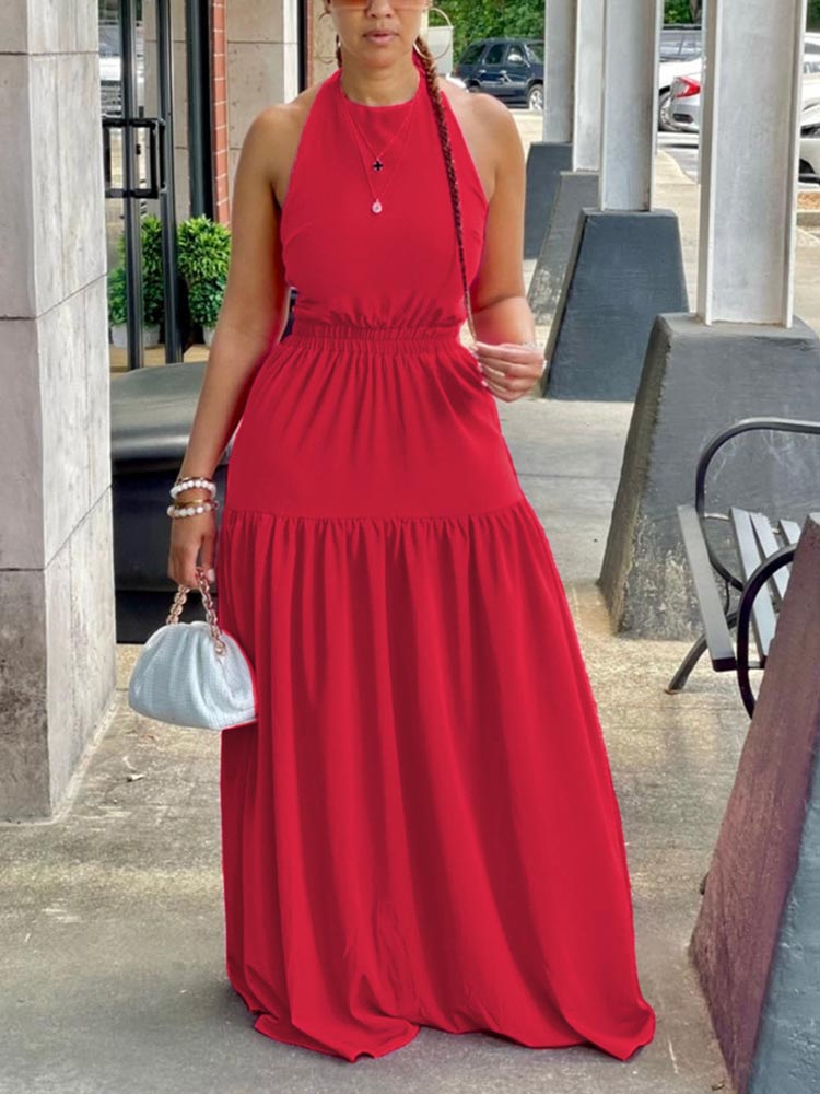 Woman wearing a red halter neck maxi dress with an elasticated waist and tiered skirt, holding a white clutch bag.