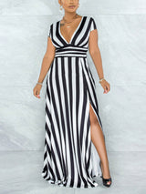 Woman wearing a black and white striped maxi dress with a V-neck and high slit, standing against a marble wall.