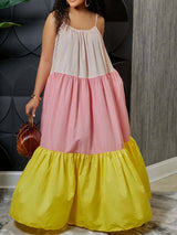 Woman in a colorful tiered maxi dress with spaghetti straps, holding a woven handbag. The dress features color blocking in light pink, pastel pink, and yellow.