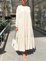 Woman wearing a long, cream-colored tiered maxi dress with long sleeves and a white handbag.