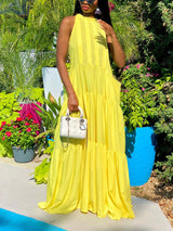 Woman in a yellow tiered maxi dress with a halter neckline, holding a white handbag.